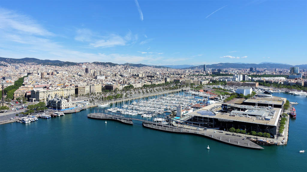 Blick aus der Gondel auf den alten Hafen, in dem Selgelboote liegen, das Maremagnum, Aquarium sowie die Stadt und die Promenade.