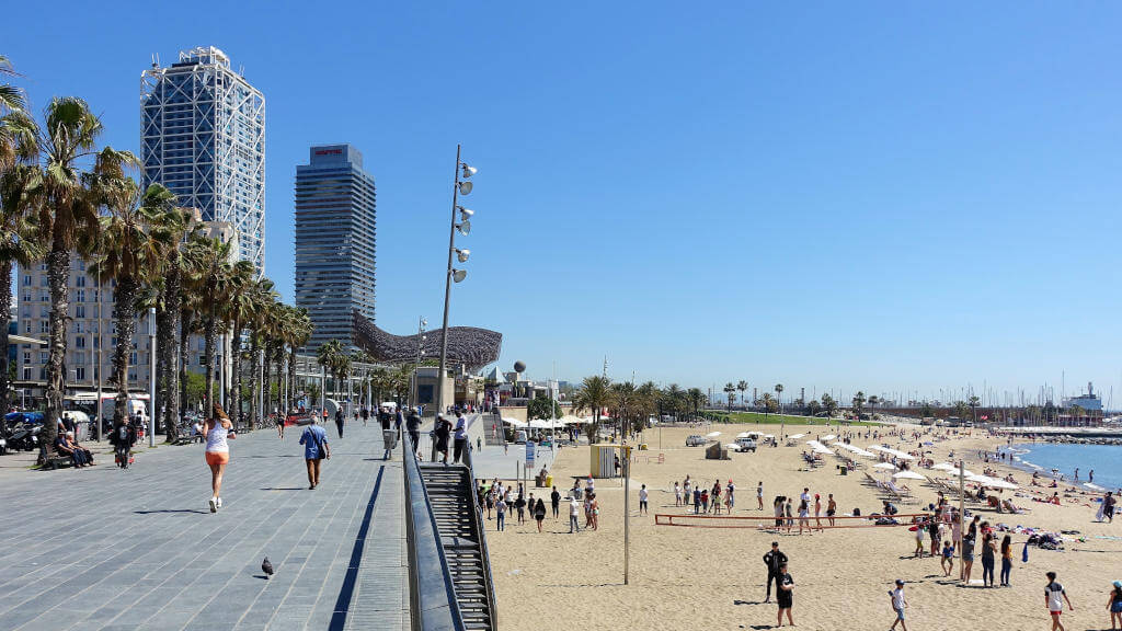 Großer Sandstrand und Strandpromenade, außerdem zwei hohe Turmbauten und der Fisch von Frank Gehri.