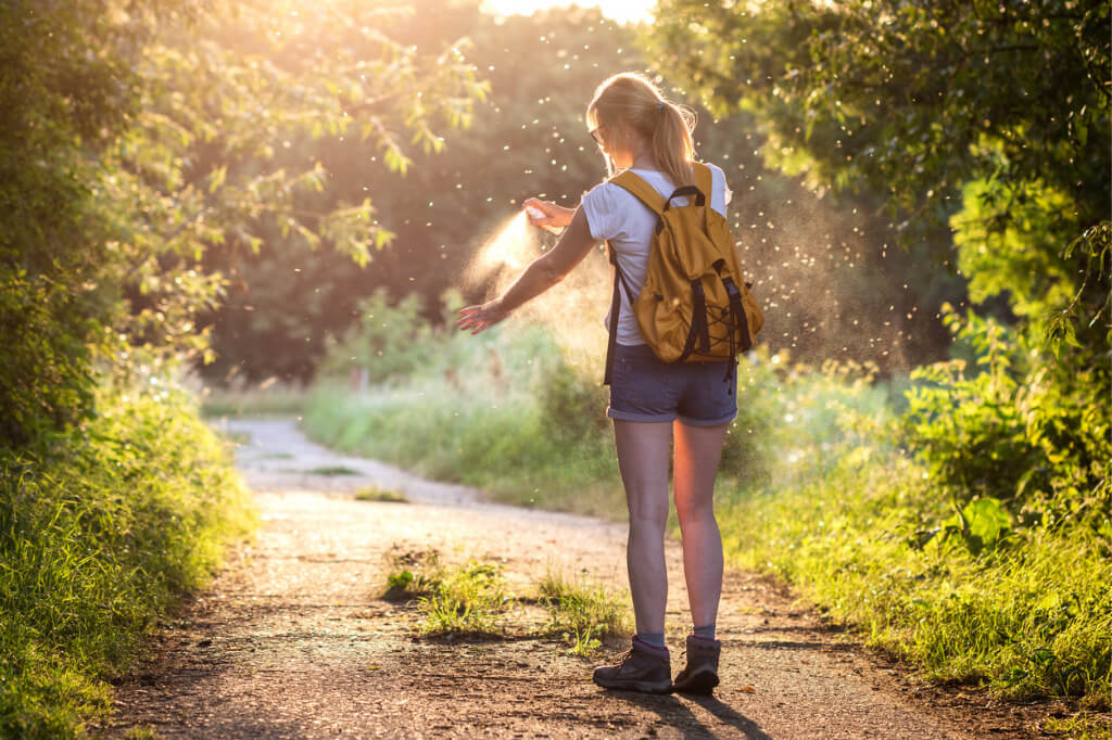 Frau auf Wanderweg, die sich in einem Schwarm voller Mücken gerade mit einem Insektenschutzmittel einsprüht